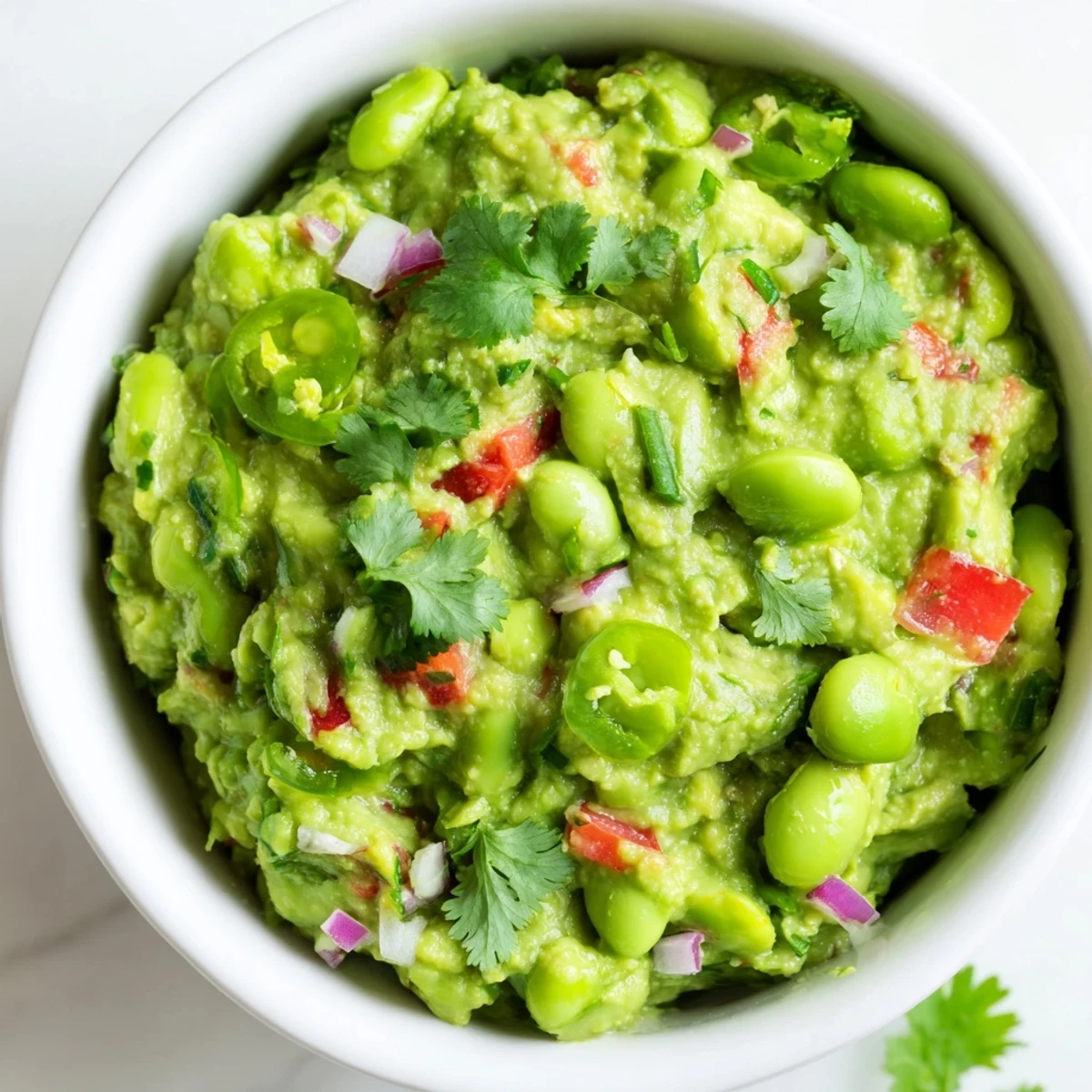 Fresh Edamame Guacamole, a rich dip with visible chunks of tomato and red onion, serving suggestion.