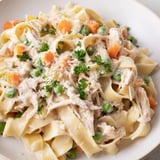 Dieses helle Frühlings-Hühnchen-Nudel-Skillet zeigt cremige Nudeln mit zartem Hühnchen, grünen Erbsen und bunten Karottenstücken, die im Kochtopf dampfen.