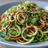 Helle Schüssel mit Spiralgemüse, übergossen von einem würzigen Sesam-Ginger-Dressing und mit gerösteten Erdnüssen bestreut.