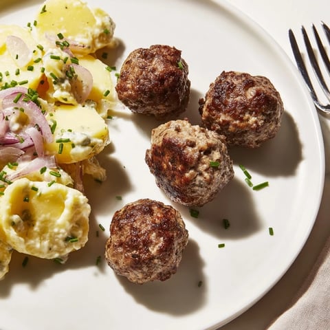 Zarte, würzige Fleischbällchen serviert mit cremigem Kartoffelsalat für ein herzhaftes Festmahl.  