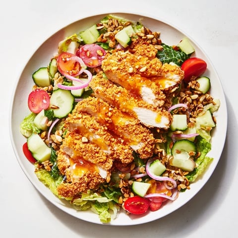 Goldene, knusprige Chicken-Strips in heißem Honig auf einem Bett aus frischem Römersalat mit knusprigen Samen.