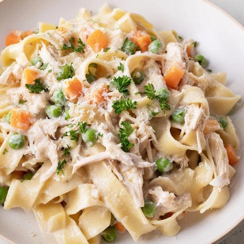 Dieses helle Frühlings-Hühnchen-Nudel-Skillet zeigt cremige Nudeln mit zartem Hühnchen, grünen Erbsen und bunten Karottenstücken, die im Kochtopf dampfen.