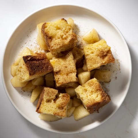 Warm bread pudding with apples and cinnamon, showing soft fruit and a golden baked crust glistening invitingly.