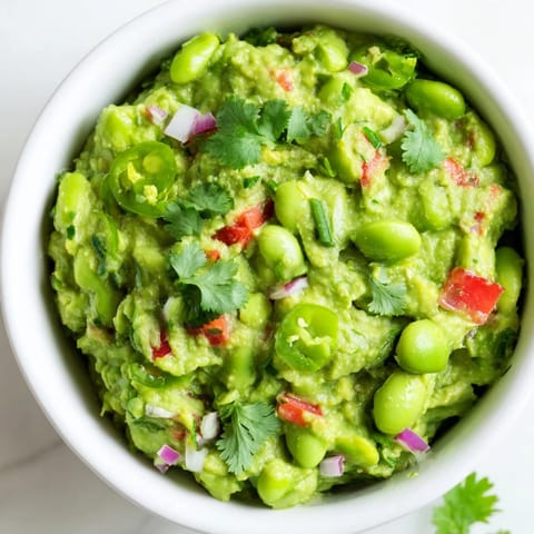 Fresh Edamame Guacamole, a rich dip with visible chunks of tomato and red onion, serving suggestion.
