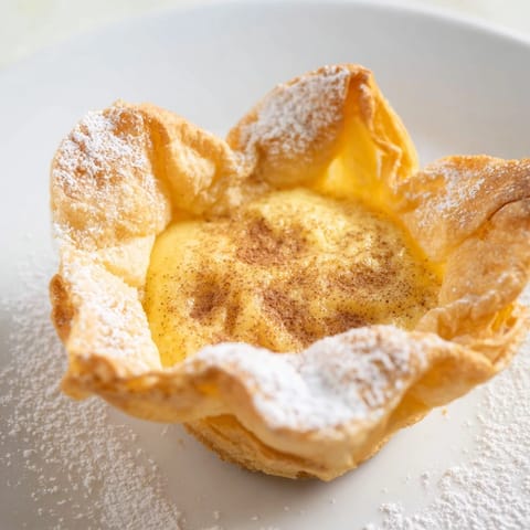 Warm, cinnamon dusted Portuguese egg tarts ready to enjoy, a classic dessert favorite.