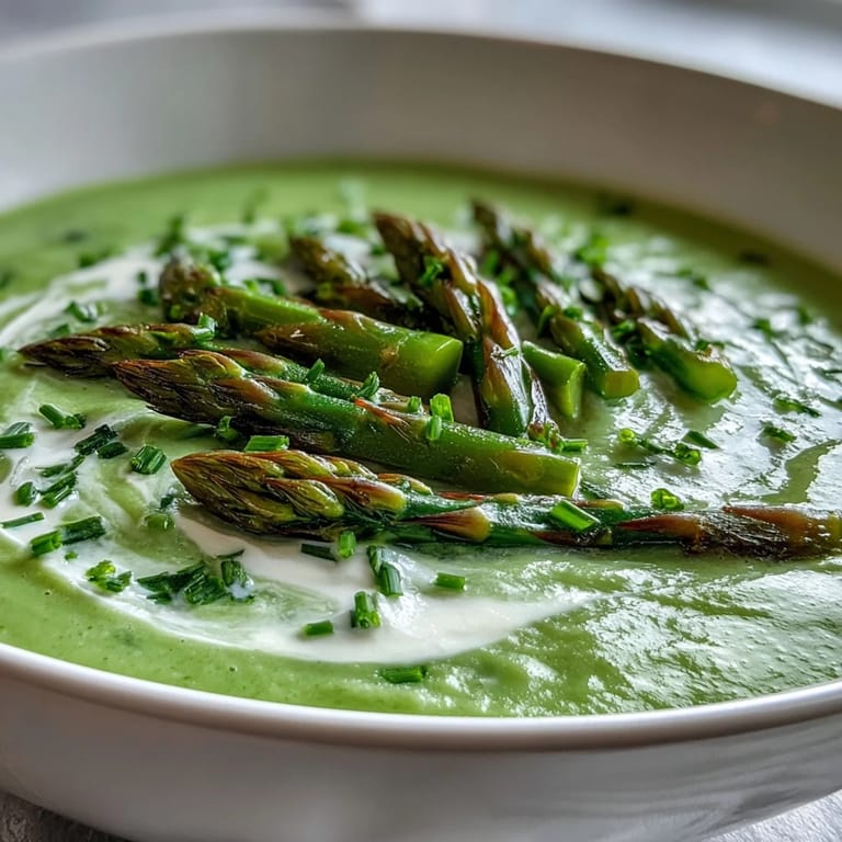 Silky blended asparagus soup in a white ceramic cup, finished with a swirl of cream.