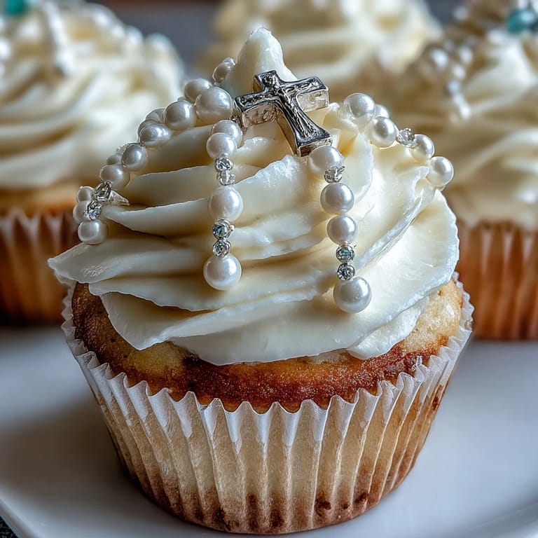 Zarte Mini-Vanille-Cupcakes mit glatter Buttercreme und Fondant-Rosenkranz-Verzierungen für eine festliche Erste Kommunion.